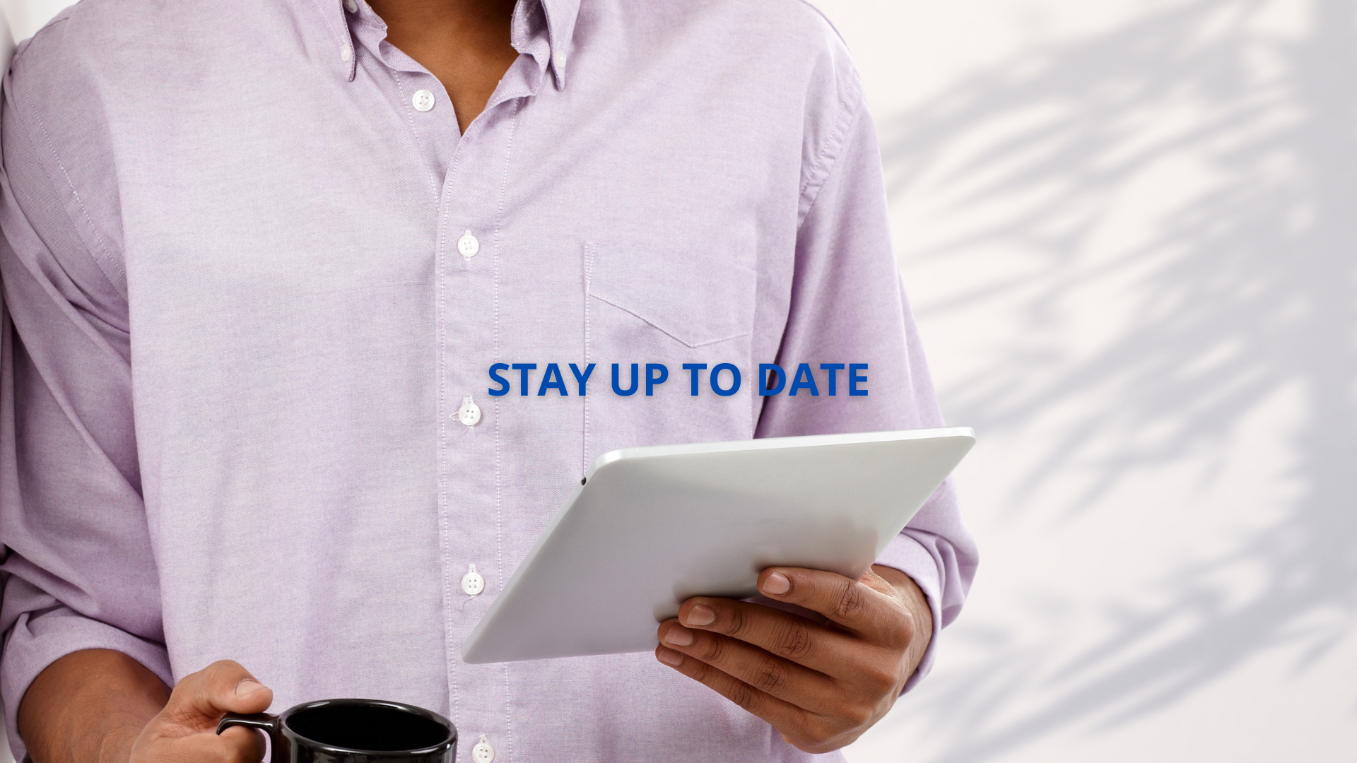 A Black man scrolling through a tablet while drinking a beverage in a mug